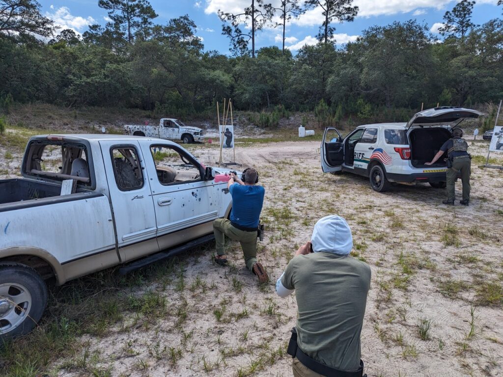 man kneeling behind shot car shooting a handgun
