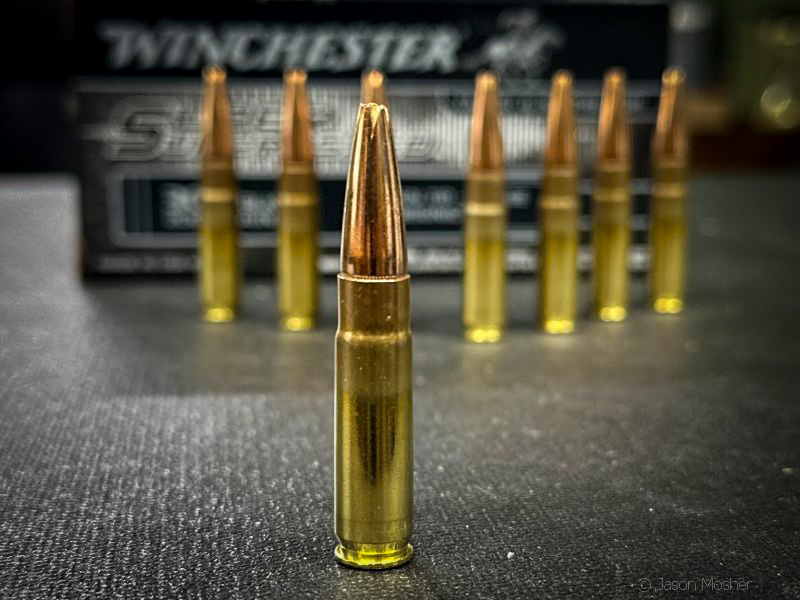 A brass and copper cartridge, standing up on a grey surface with more bullets behind it.