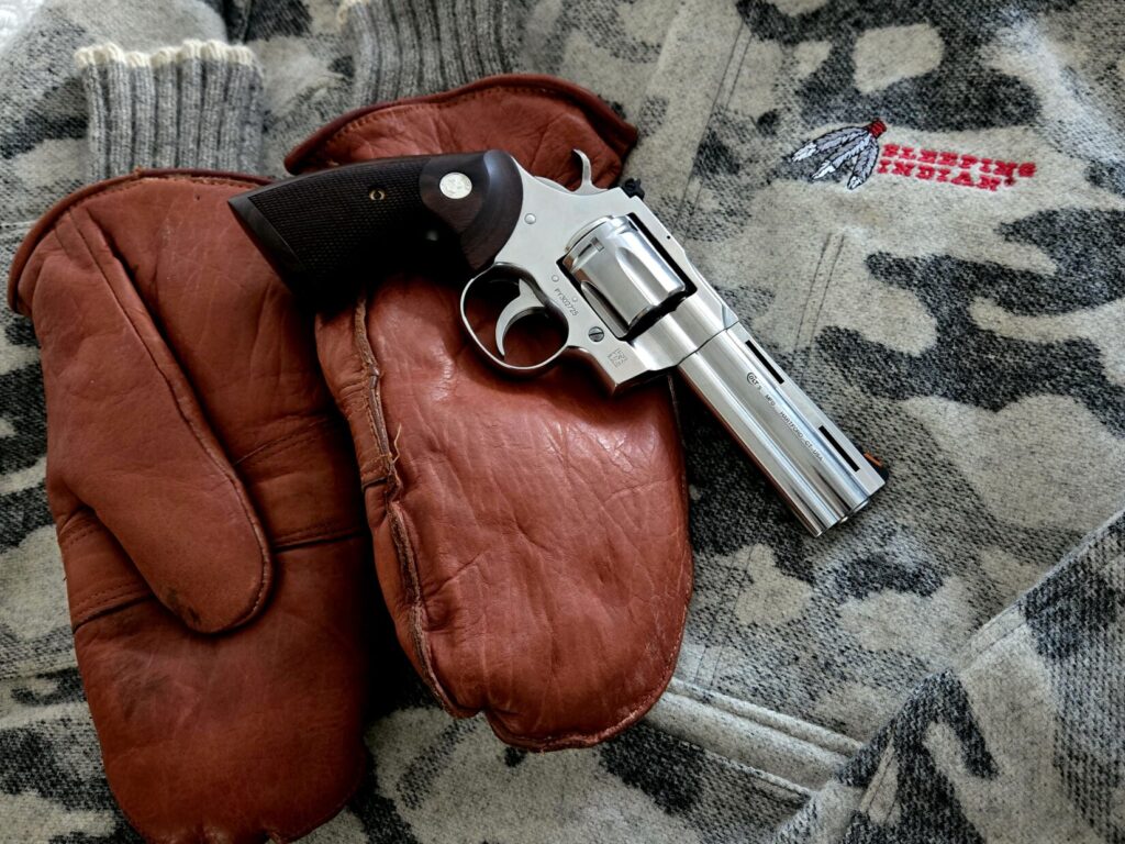 A silver revolver on top of leather mittens with a wool parka backdrop