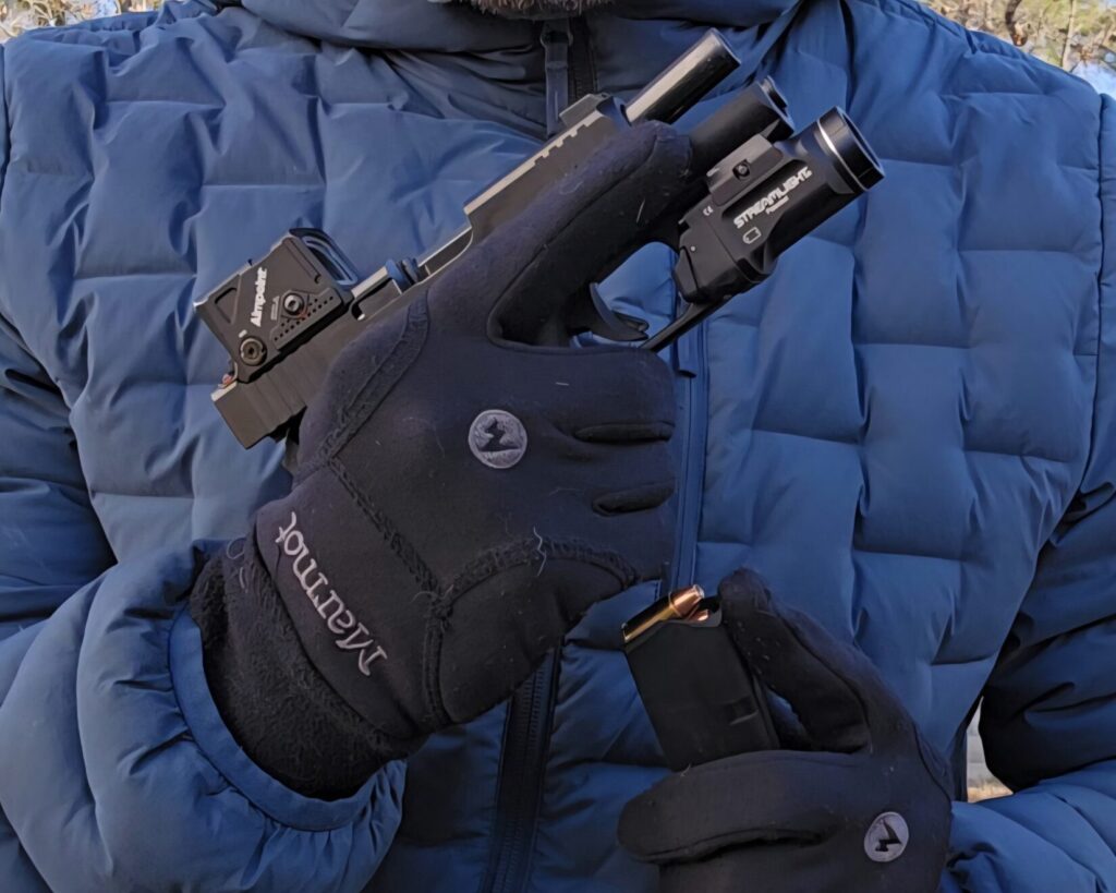 A pistol being reloaded by a man in a blue jacket and black gloves
