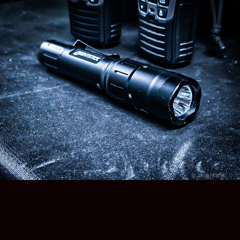 A black flashlight laying on a black table. 