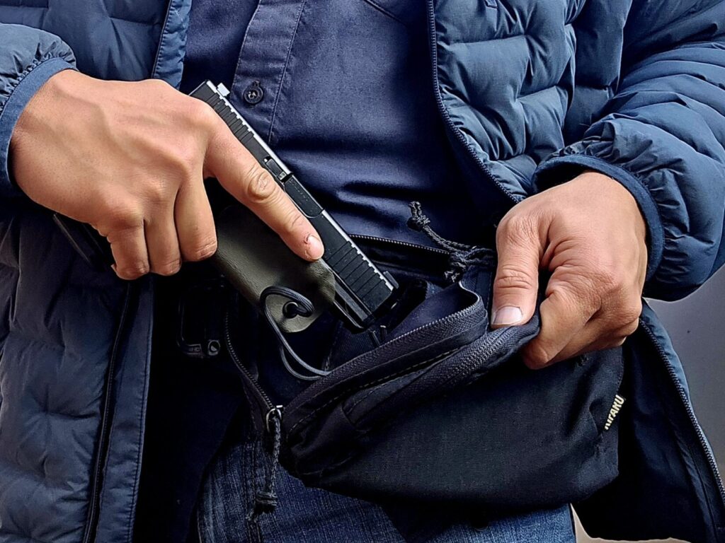 A man in a blue jacket draws a Glock pistol from a fanny pack