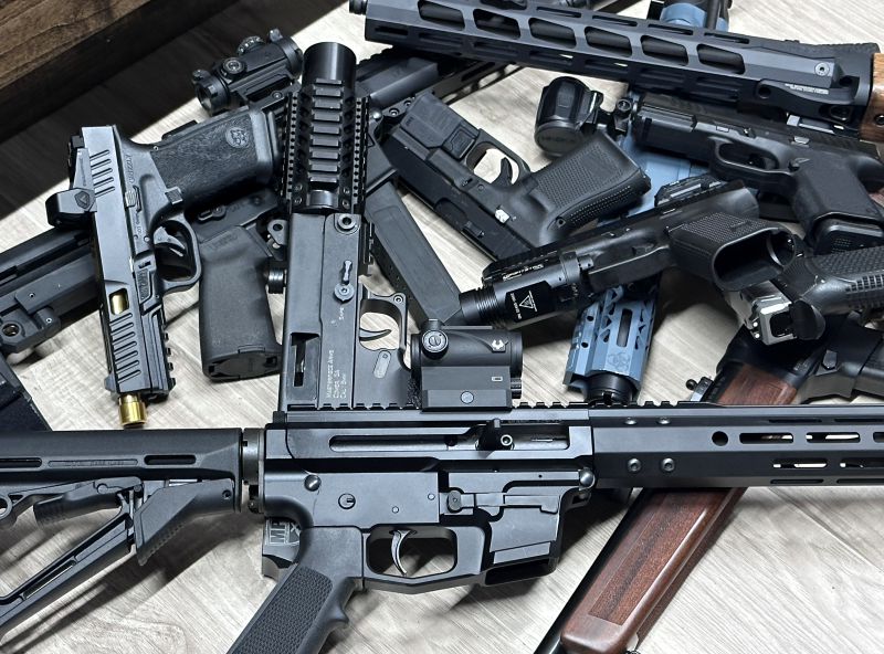 Multiple firearms in a pile on the ground. 