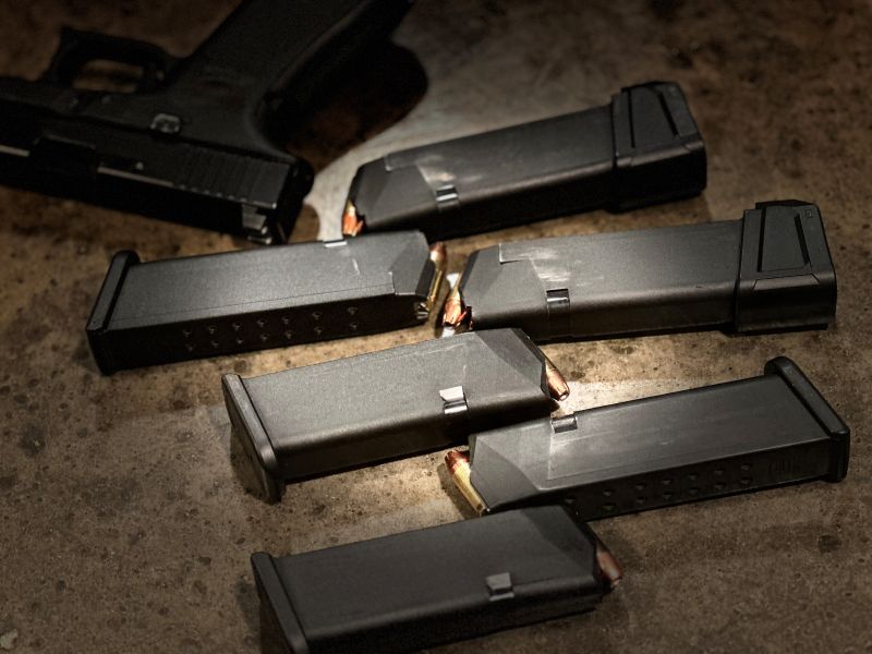 Multiple black Glock magazines with ammo in them on a wood table. 