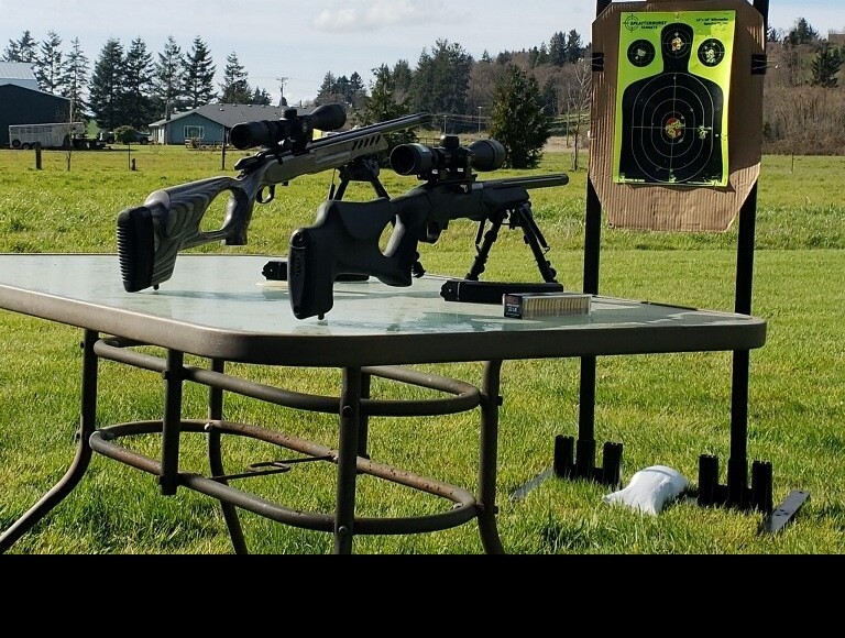 two scoped rifles on a table outsite, with target stand closeby