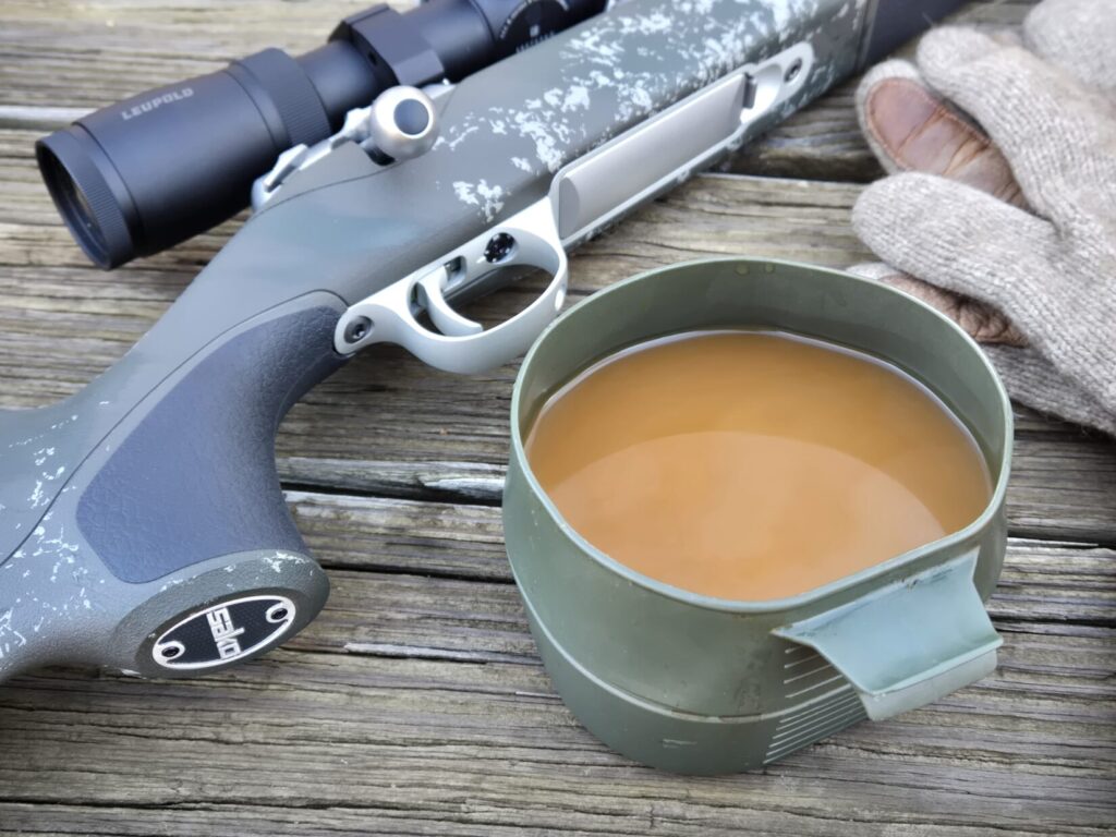 A rifle on a table with a set of gloves and a cup of coffee