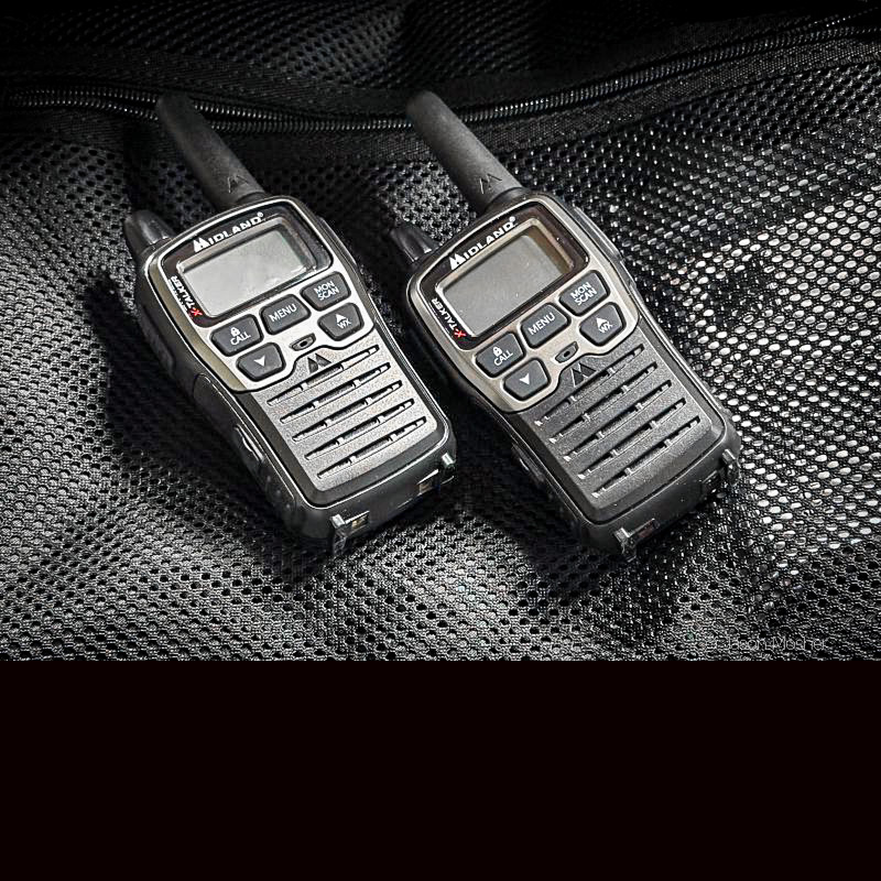 Two small walkie-talkies in front of a black bag. 