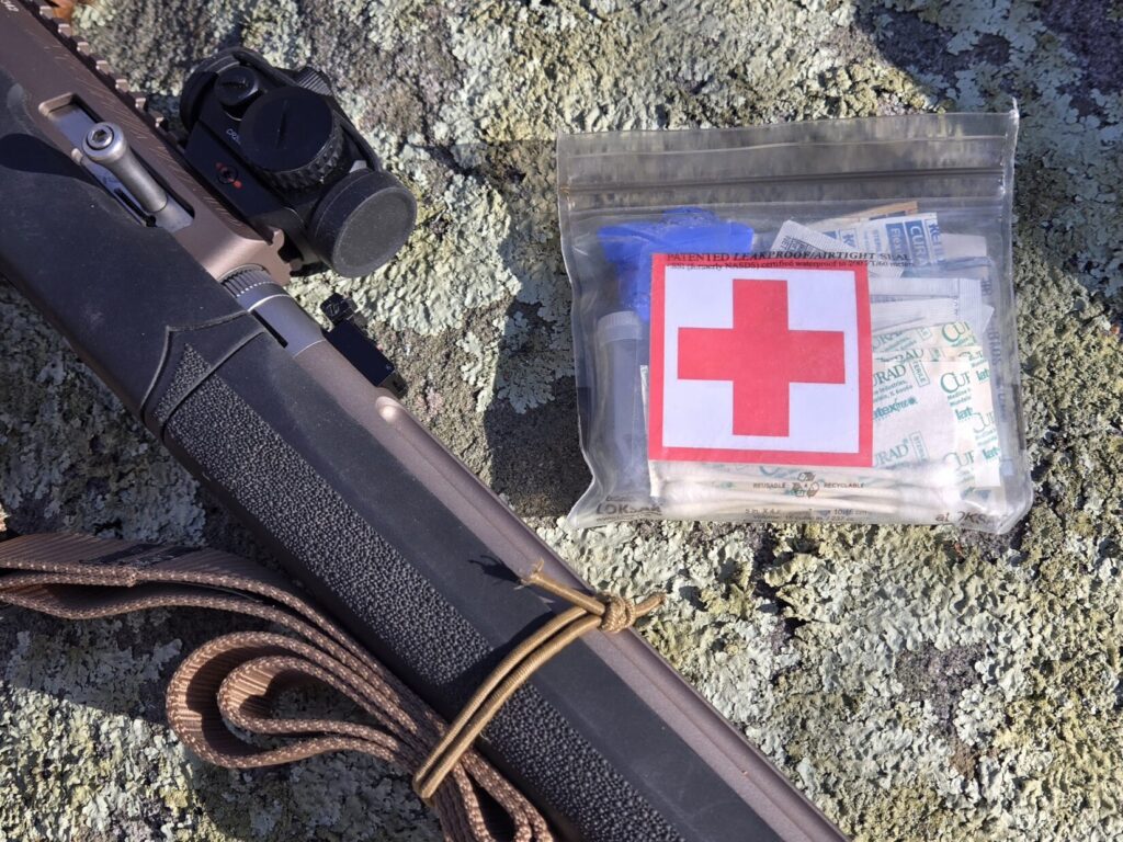 A first-aid pouch next to a rimfire rifle with red dot
