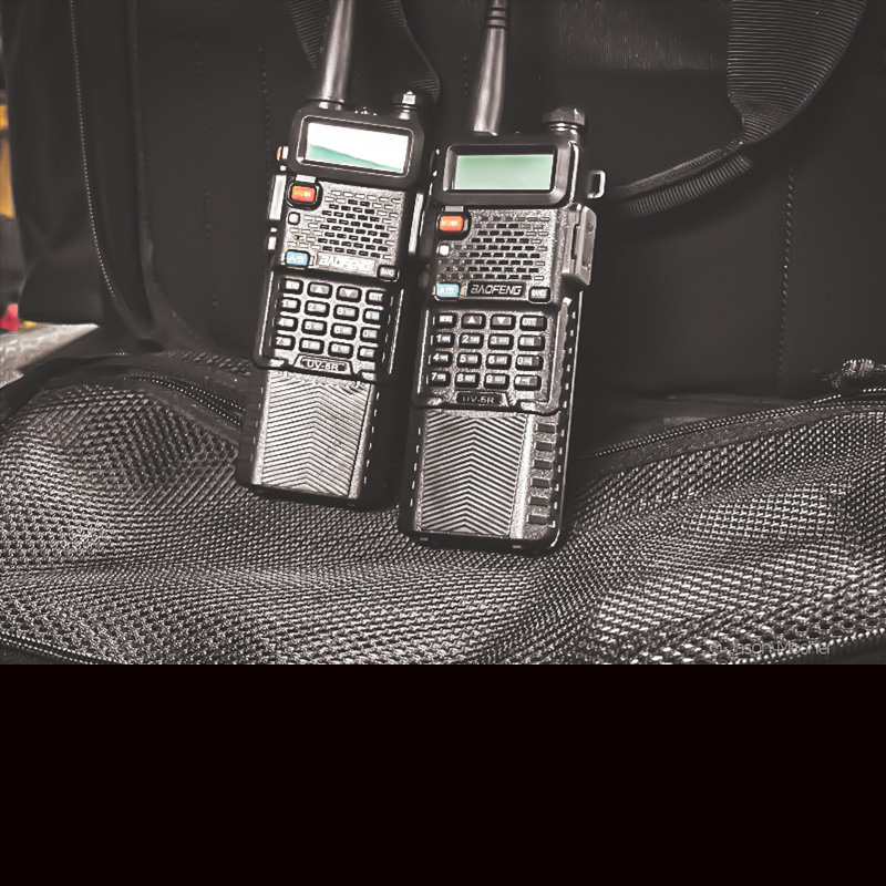 Two black radios in front of a black bag. 