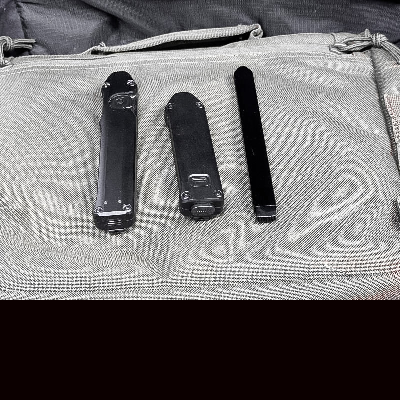 Three black flashlights laying next to each other on a grey surface. 