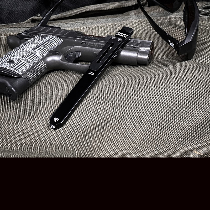 A thin black flashlight resting on a small compact handgun. 