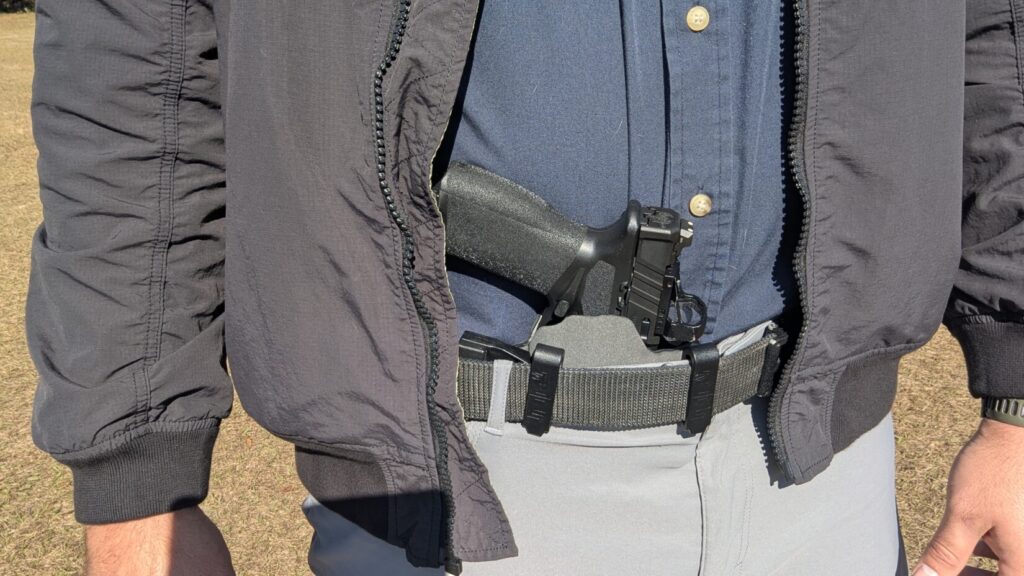 Close-up of a pistol holstered in the appendix position, revealed by an open jacket.