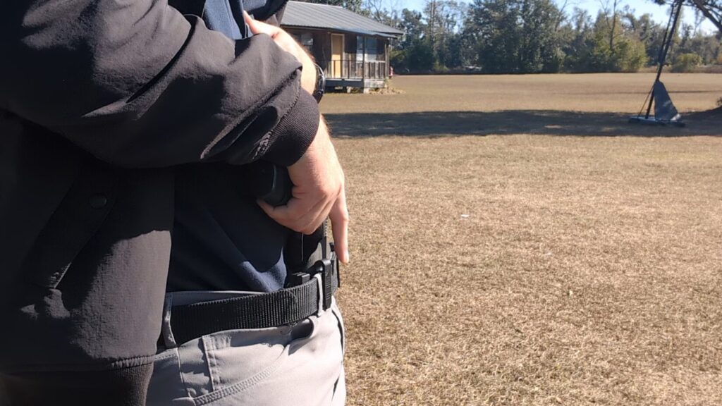 Man's hand on a pistol in appendix carry, jacket still covering.