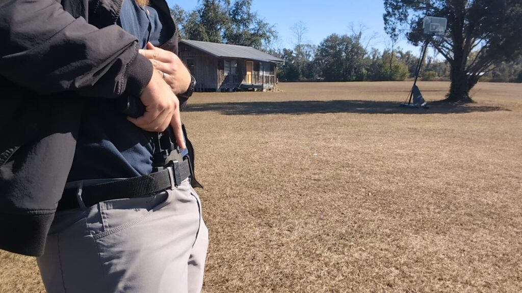 Close-up of man gripping pistol in appendix holster under a jacket.