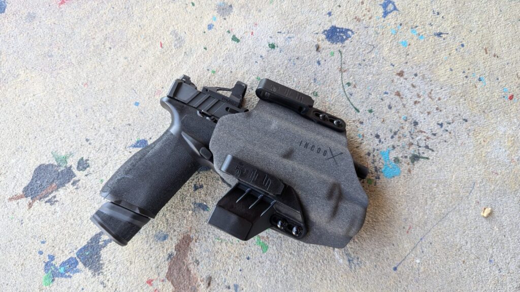 Pistol with a red dot sight in an INCOG X holster with a spare magazine carrier, lying on concrete