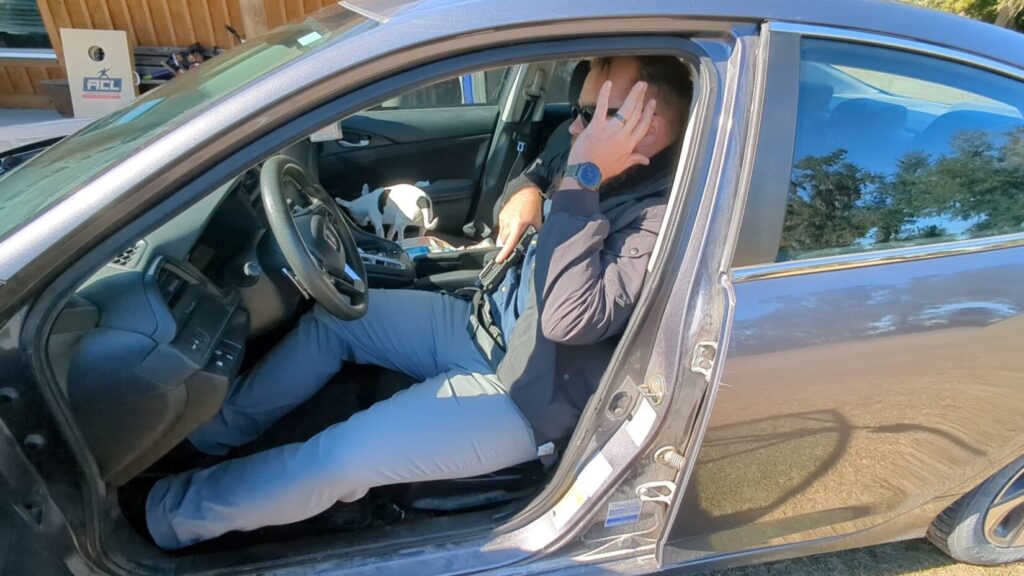 Man seated in car drawing pistol from appendix carry.