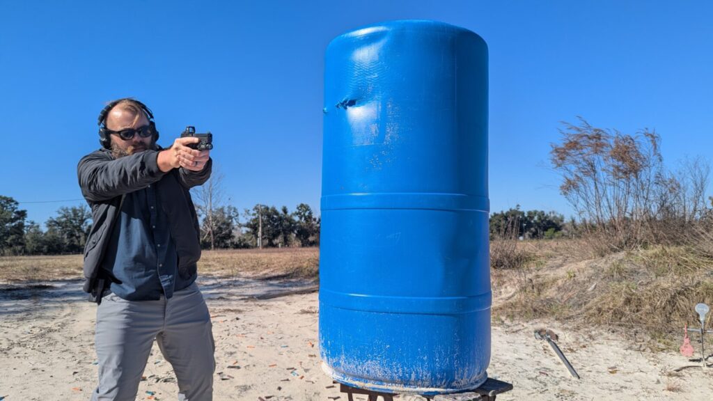 Shooter engaging target from behind a large blue barrel cover.