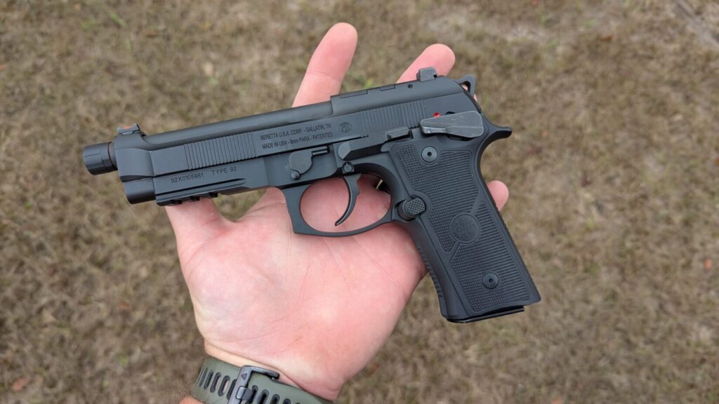 Hand holding a side view of a Beretta 92 pistol showing the slide markings.