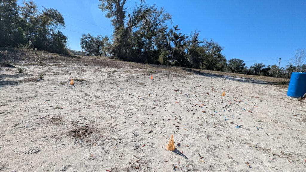 Outdoor shooting range with cones marking positions and shell casings scattered.