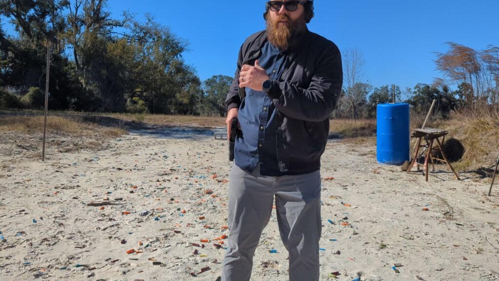 Shooter drawing pistol from concealment at outdoor range.