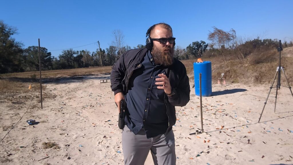 Shooter drawing pistol from concealment at outdoor range.