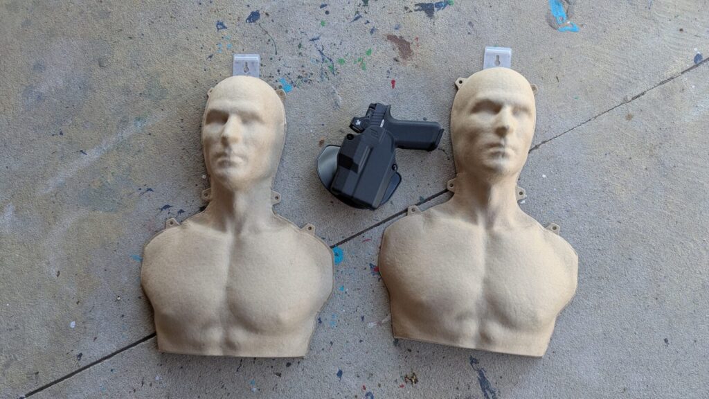 Two target silhouettes and a gun in holster on concrete.