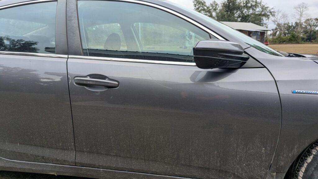 Close-up of the dirty front door and side mirror of a dark gray sedan (Honda Insight Hybrid).