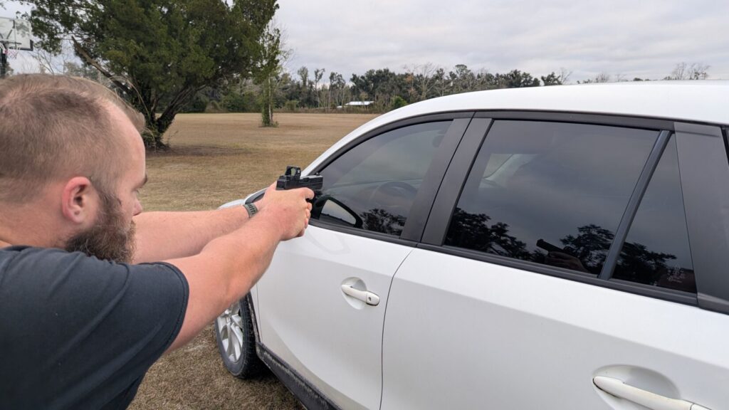 Man aiming a pistol over the roofline/window edge of a white SUV door.