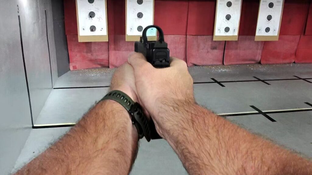 First-person view of a shooter aiming a pistol with a red dot sight downrange at multiple targets.