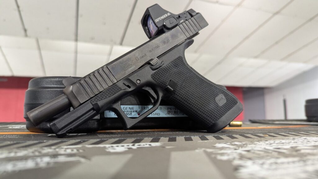 Low-angle view of a Glock 17 Gen 6 with a red dot sight, set on a dark mat, with the barrel exposed.