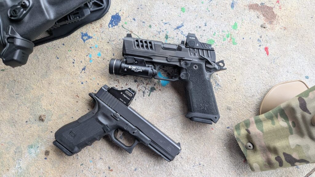 Overhead view of a Glock 17 and a Staccato HD pistol, both customized with optics and lights, on concrete.