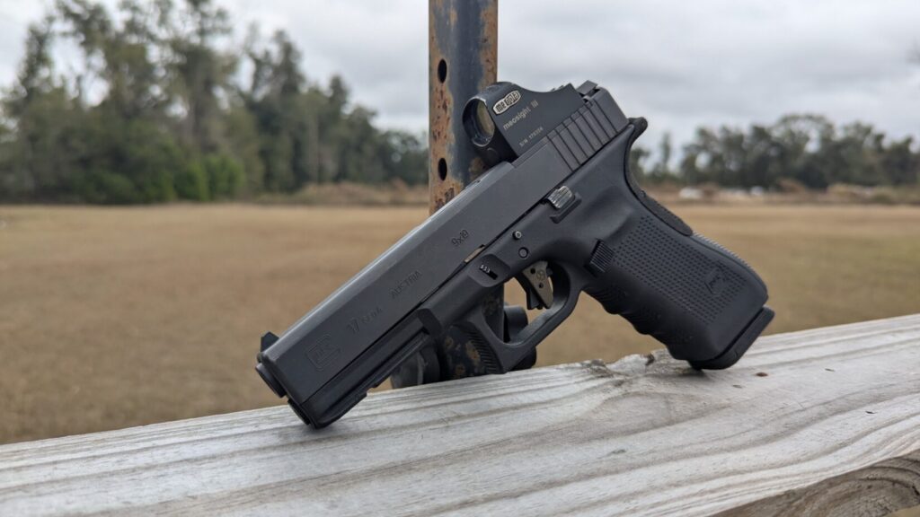 Side profile of a customized Glock 17 9x19 pistol with a red dot sight, resting on a wooden fence post.