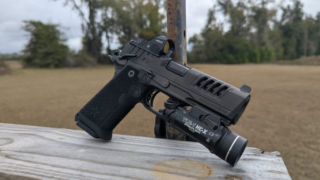 Side profile of a StaccatoHD, red dot sight, and Streamlight TLR-1 weapon light, resting on a wooden fence post.