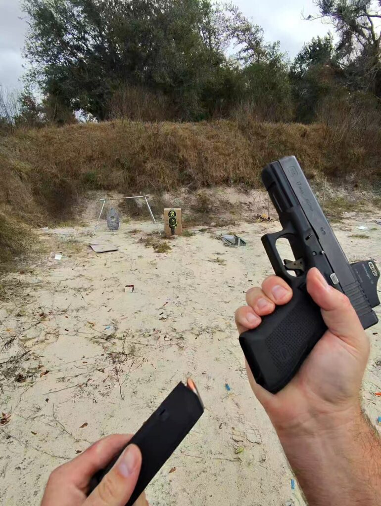 Shooter's hands performing a magazine change on a Glock 17 pistol at an outdoor shooting range.