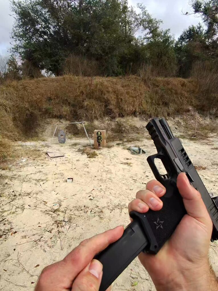 Shooter's hands performing a magazine change on a Staccato HD pistol at an outdoor shooting range.