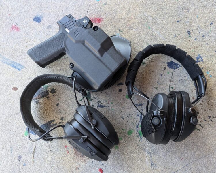 Safariland hearing protection muffs next to a handgun in a holster.