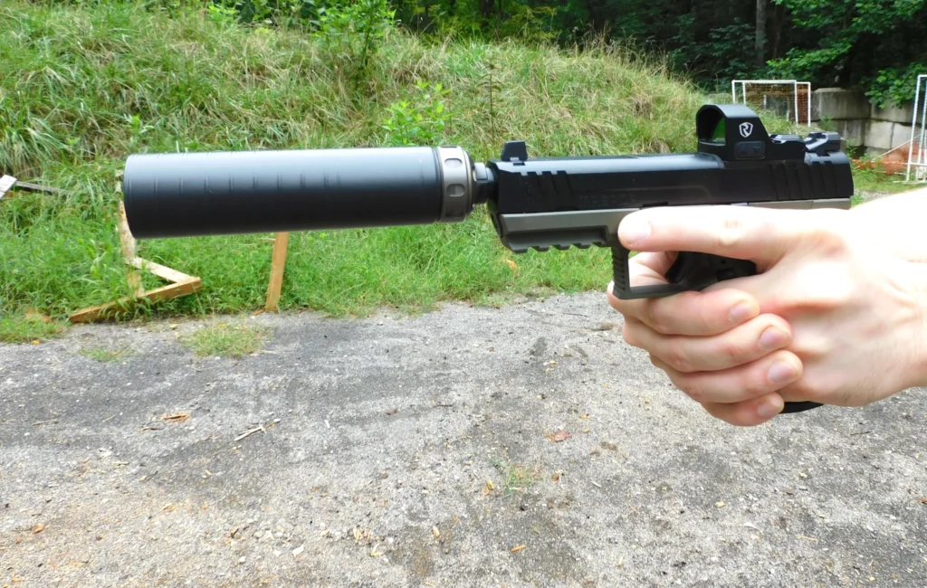 Man firing a semiautomatic pistol with a red dot and a silencer