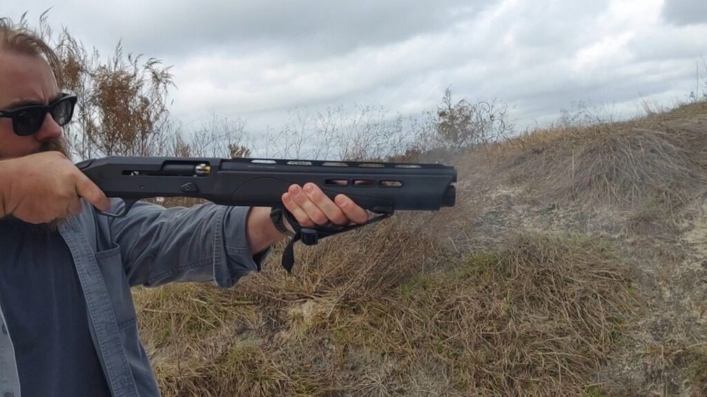 Side view of man firing a semi-automatic shotgun  outdoors.