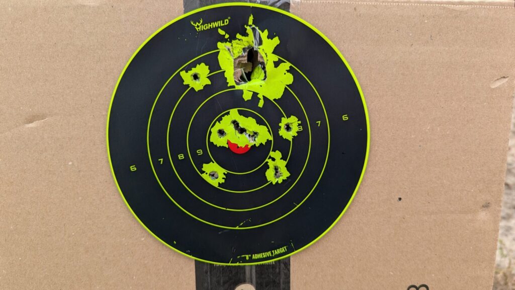 Tight shotgun pattern on a black and neon yellow circular adhesive target with center hits.