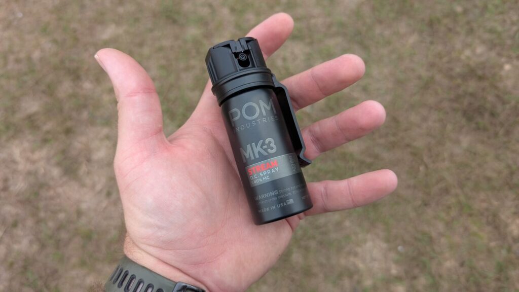 Hand holding a compact black POM Industries MK3 Stream O.C. Spray canister.
