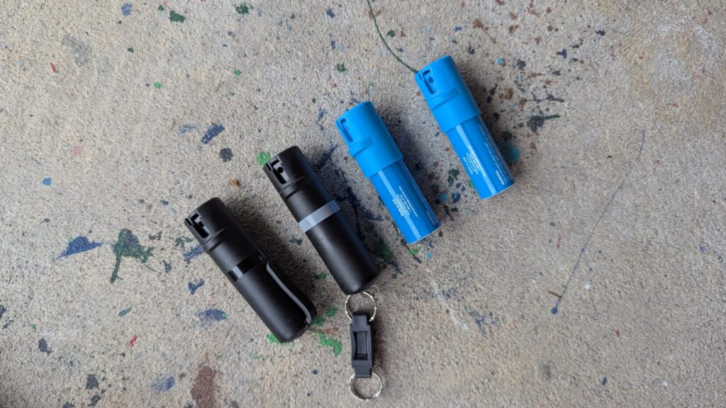 Four POM pepper spray units, two blue practice units and two black live units, on a keychain.