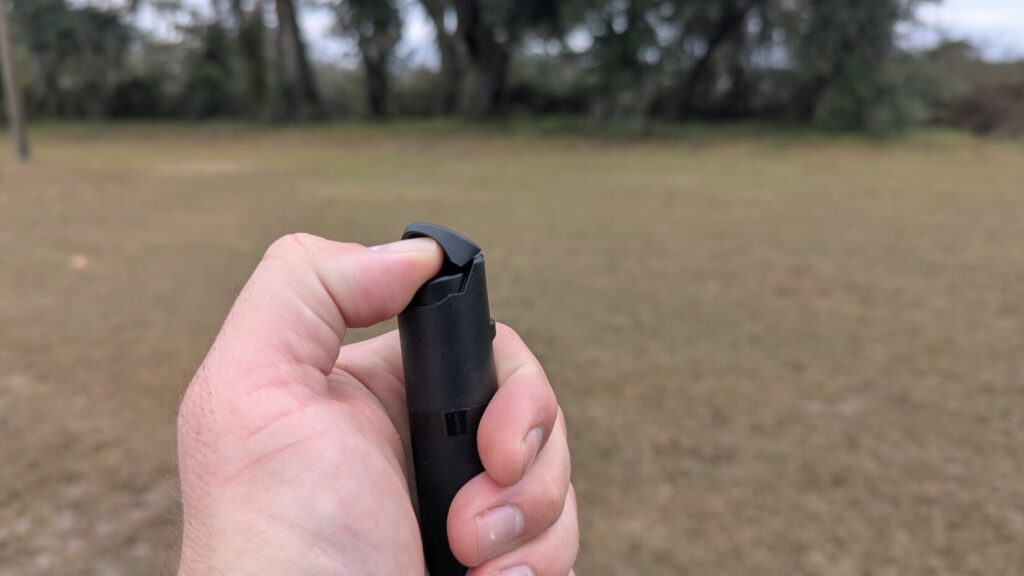 Close-up of a hand pressing down on the flip-top safety cap of the black POM pepper spray.