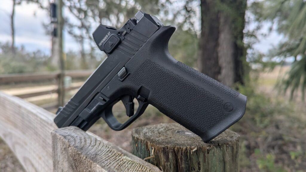 Black Ruger RXM pistol with a red dot sight resting on a wooden fence post in an outdoor setting.