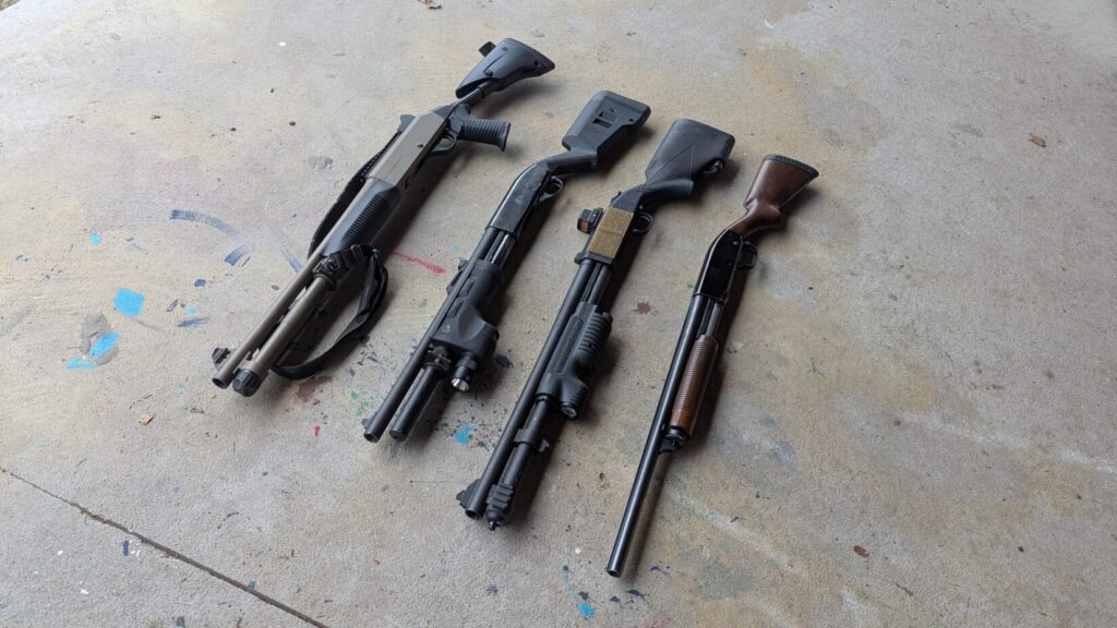 Four shotguns with varying accessories laid on a concrete slab