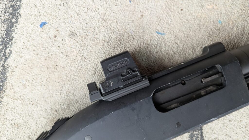 Close-up of a Holosun red dot sight mounted on a shotgun receiver.