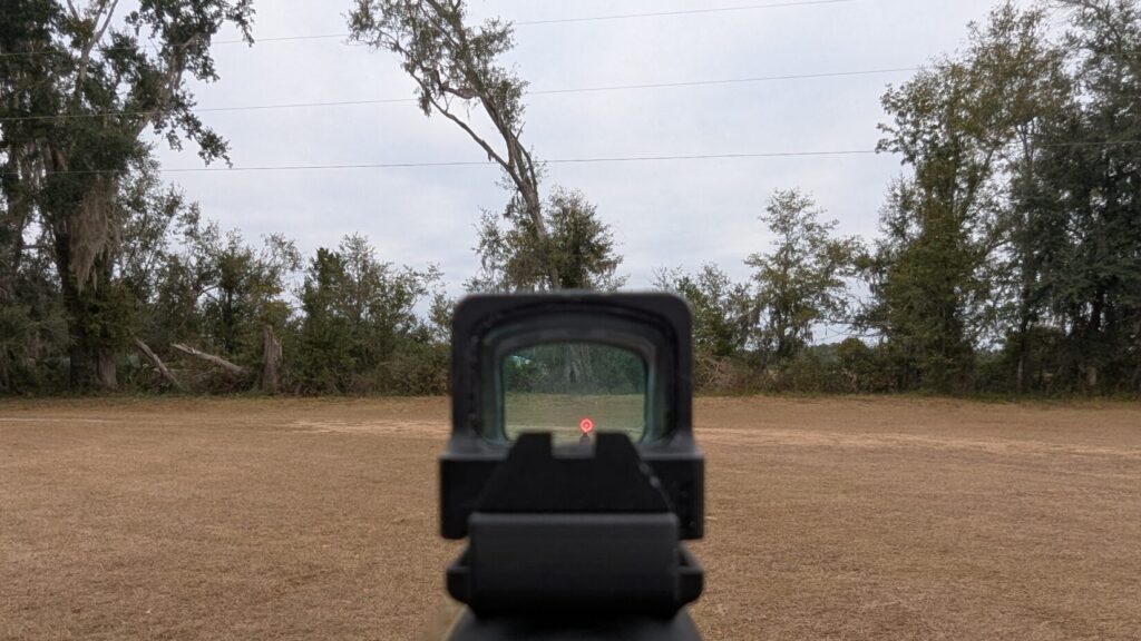 Red dot sight view with illuminated reticle aimed outdoors
