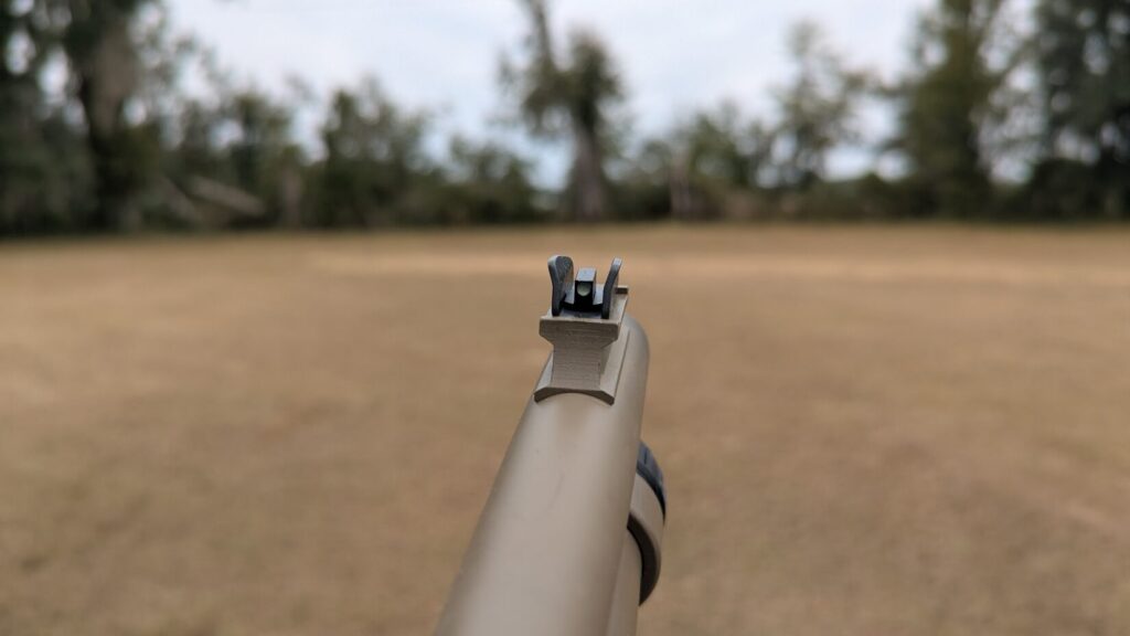 Close-up of a tan shotgun receiver with an attached Picatinny rail and an adjustable iron sight.