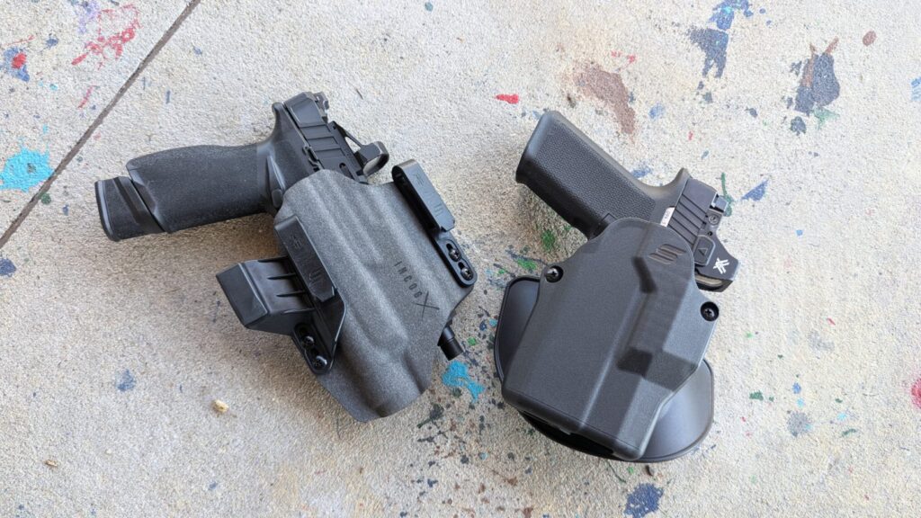 Two black pistols holstered in Kydex holsters on a concrete surface.