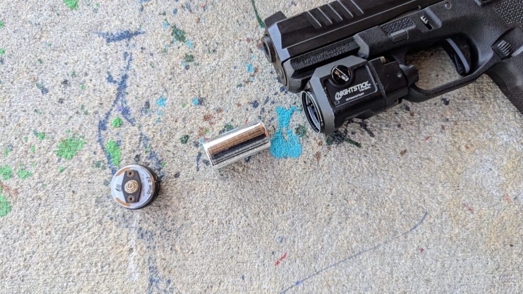 A pistol-mounted light with its battery removed, next to the light's head. .