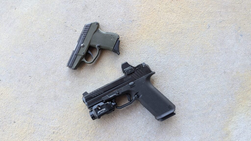 large black handgun with a light/optic next to a small green handgun.